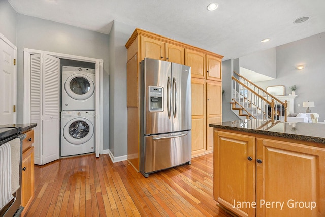 kitchen featuring stacked washer and clothes dryer, light brown cabinets, light wood-type flooring, stainless steel fridge, and dark stone counters