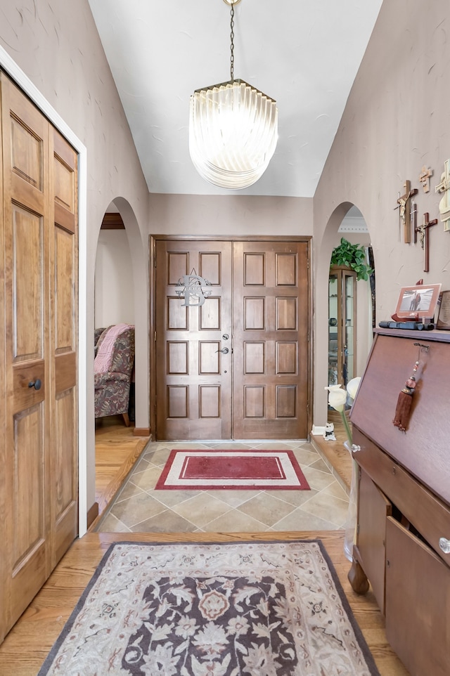 entrance foyer featuring light wood finished floors, arched walkways, and vaulted ceiling