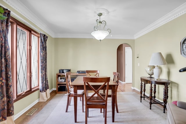 dining space with arched walkways, ornamental molding, visible vents, and light wood-style floors