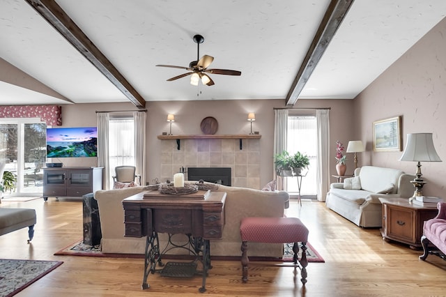 living room with light wood-style floors, a wealth of natural light, a fireplace, and lofted ceiling with beams