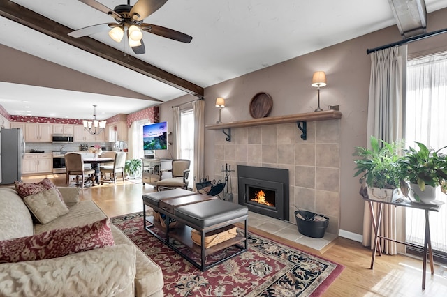 living room featuring vaulted ceiling with beams, light wood-style floors, a tile fireplace, and a healthy amount of sunlight