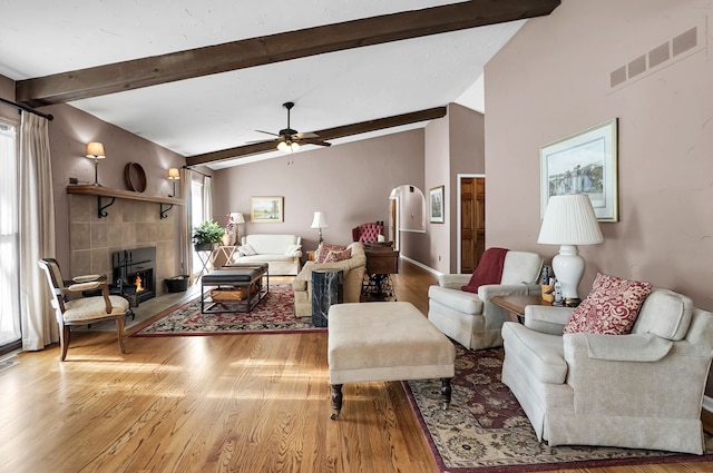 living room featuring a fireplace, visible vents, lofted ceiling with beams, a ceiling fan, and wood finished floors