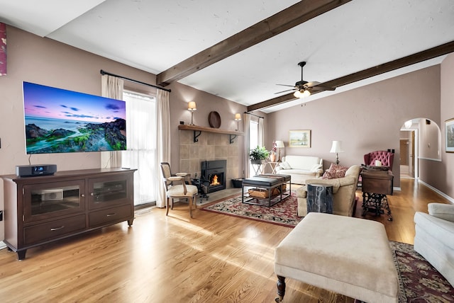 living room with lofted ceiling with beams, ceiling fan, arched walkways, a fireplace, and light wood-type flooring