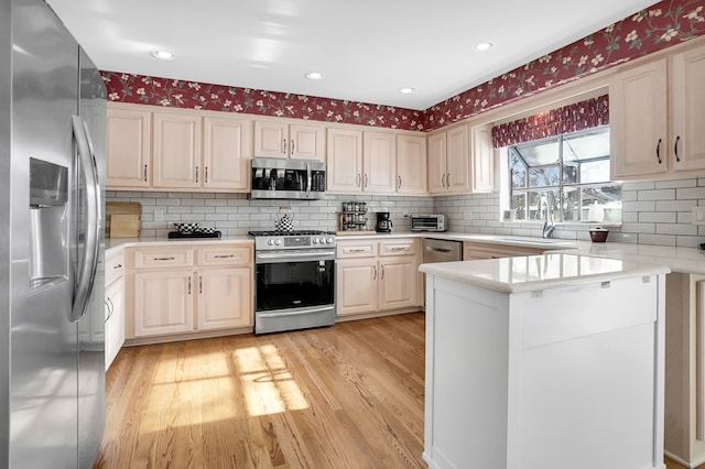 kitchen featuring stainless steel appliances, light countertops, light wood-style flooring, a sink, and a peninsula