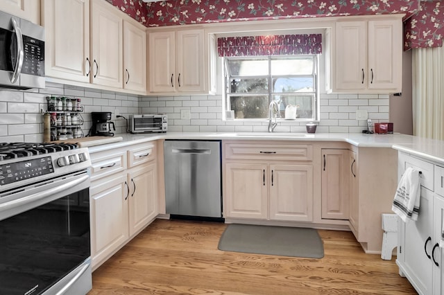 kitchen featuring appliances with stainless steel finishes, light wood-style floors, a sink, and wallpapered walls