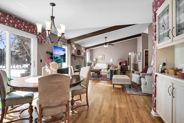 dining area featuring arched walkways, lofted ceiling with beams, light wood finished floors, and ceiling fan with notable chandelier