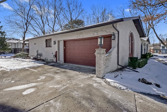 view of snow covered exterior with a garage, driveway, and brick siding