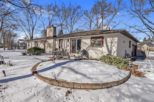 snow covered back of property with brick siding and a chimney