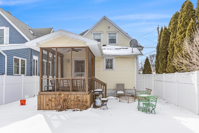 snow covered back of property with a sunroom and ceiling fan