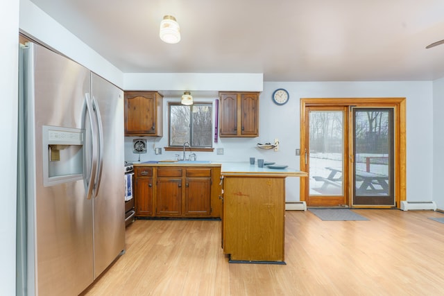 kitchen featuring light countertops, appliances with stainless steel finishes, a baseboard heating unit, a sink, and light wood-type flooring