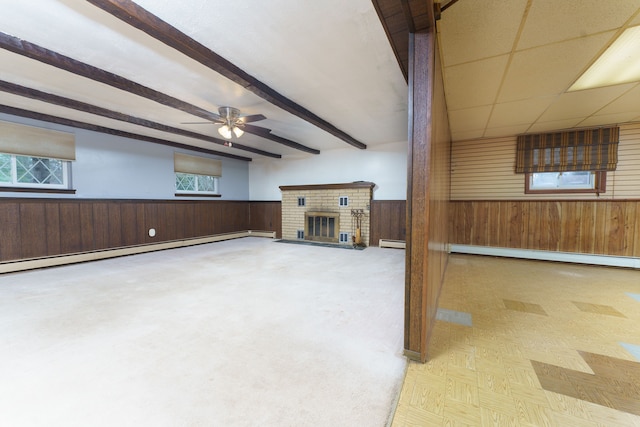 unfurnished living room featuring wooden walls, wainscoting, a baseboard radiator, beamed ceiling, and a fireplace