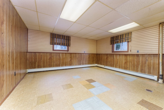 empty room with a baseboard radiator, wooden walls, and a drop ceiling