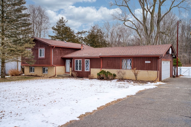 split level home with a garage, brick siding, driveway, and a shingled roof