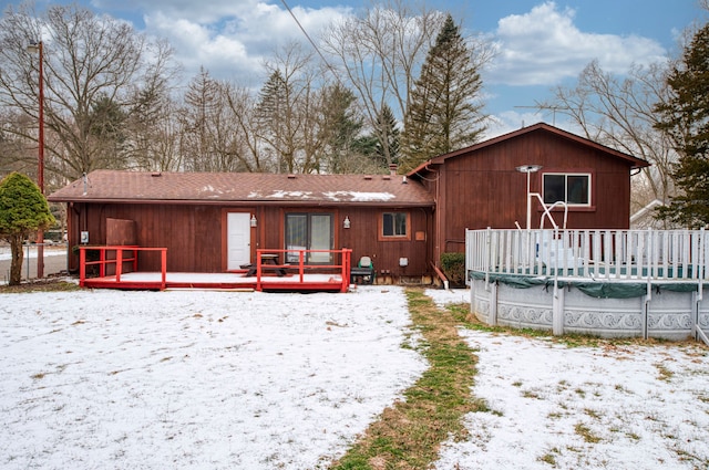 snow covered back of property with a covered pool, a deck, and roof with shingles