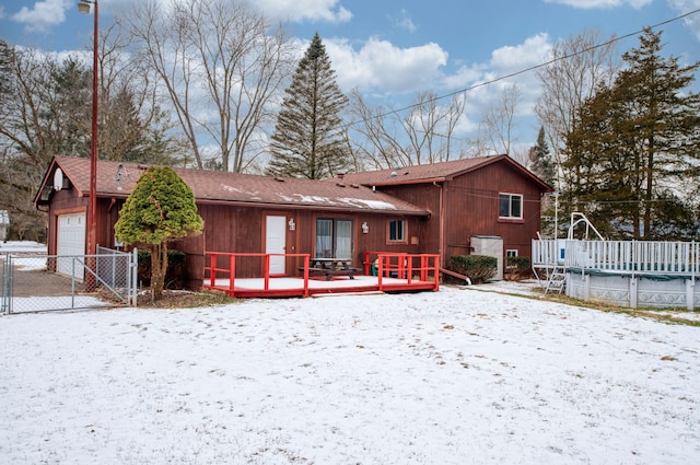 snow covered back of property featuring a covered pool, a detached garage, a gate, fence, and a deck