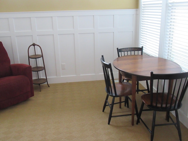 dining space featuring a wainscoted wall, a decorative wall, and light colored carpet