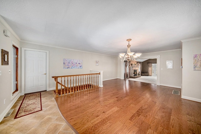 unfurnished room featuring a notable chandelier, ornamental molding, a textured ceiling, and light wood-type flooring