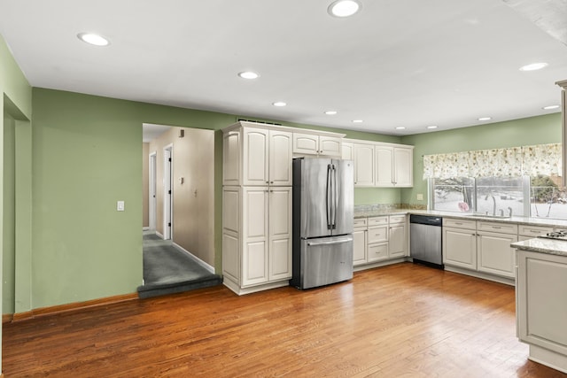 kitchen with sink, appliances with stainless steel finishes, white cabinetry, light hardwood / wood-style floors, and light stone countertops