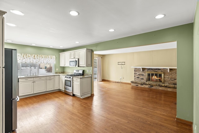 kitchen featuring sink, white cabinets, stainless steel appliances, a brick fireplace, and light wood-type flooring