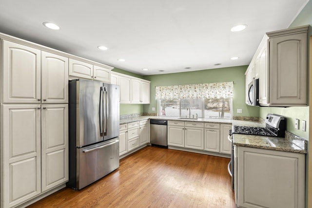 kitchen with sink, light hardwood / wood-style flooring, appliances with stainless steel finishes, white cabinets, and stone countertops