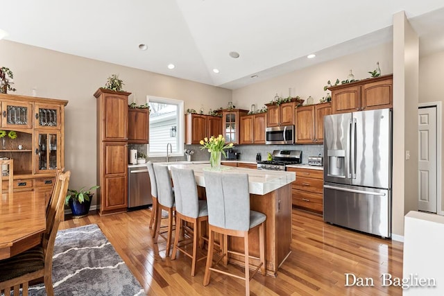 kitchen with vaulted ceiling, a kitchen island, appliances with stainless steel finishes, tasteful backsplash, and light hardwood / wood-style flooring