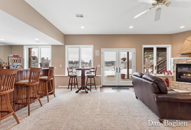 living room featuring french doors, a stone fireplace, bar area, light carpet, and ceiling fan