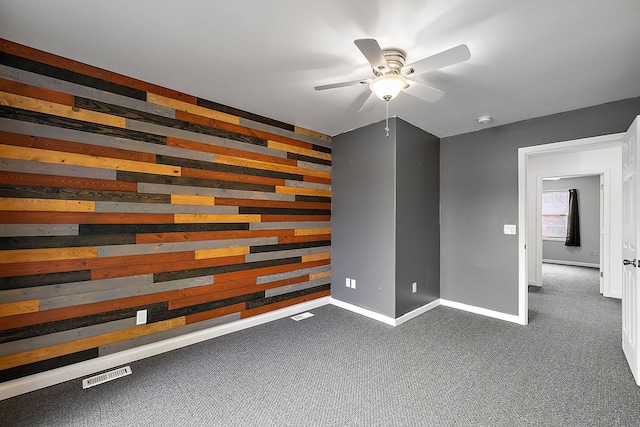 unfurnished room with ceiling fan, dark carpet, and wooden walls