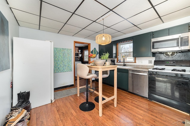 kitchen with sink, decorative light fixtures, light wood-type flooring, stainless steel appliances, and a drop ceiling