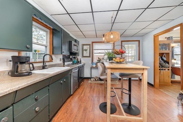 kitchen featuring pendant lighting, sink, a paneled ceiling, stainless steel appliances, and light wood-type flooring