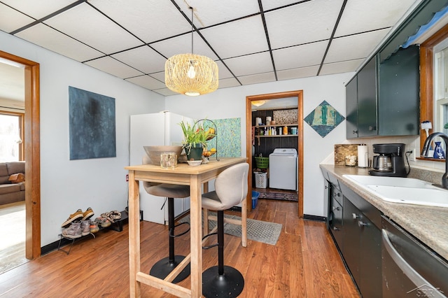 kitchen with pendant lighting, a paneled ceiling, sink, hardwood / wood-style flooring, and stainless steel dishwasher