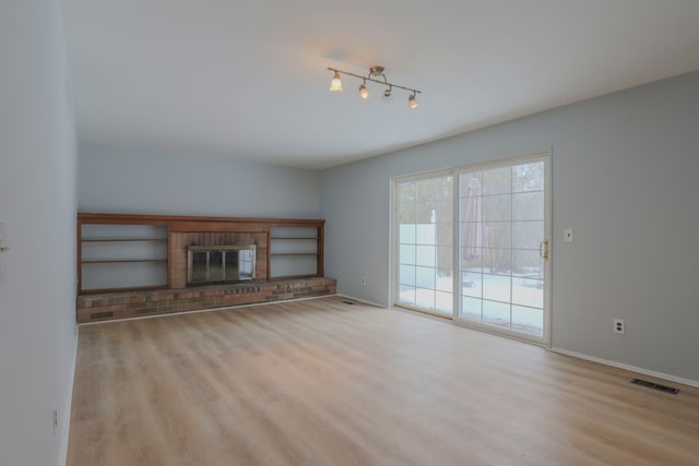 unfurnished living room with rail lighting, a brick fireplace, and light wood-type flooring