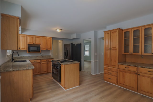 kitchen with sink, dark stone counters, light hardwood / wood-style floors, and black appliances