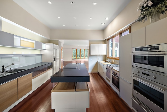 kitchen with appliances with stainless steel finishes, sink, white cabinets, dark hardwood / wood-style flooring, and decorative backsplash