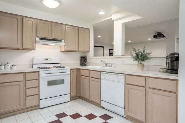 kitchen featuring sink, light brown cabinetry, and white appliances