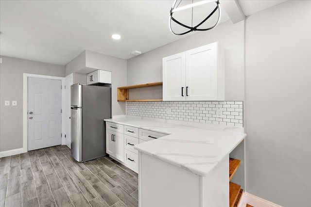 kitchen with light stone counters, stainless steel fridge, kitchen peninsula, light hardwood / wood-style floors, and white cabinets