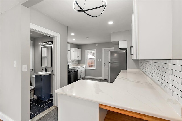 kitchen with stainless steel refrigerator, a breakfast bar, backsplash, white cabinets, and kitchen peninsula