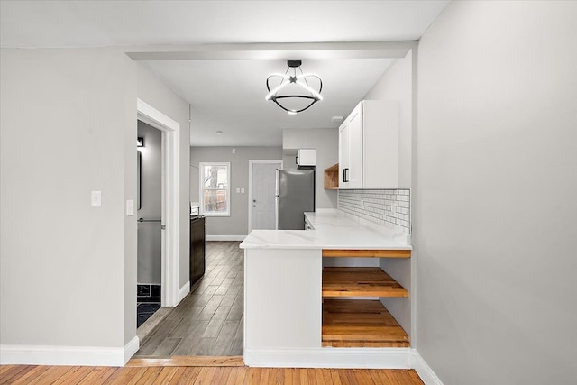 kitchen with light hardwood / wood-style flooring, stainless steel refrigerator, white cabinetry, an inviting chandelier, and tasteful backsplash