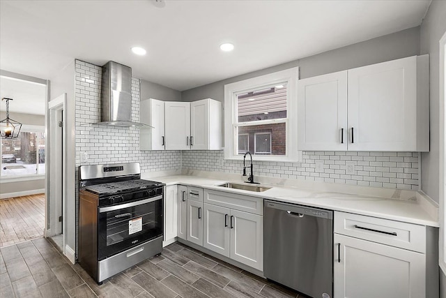 kitchen featuring wall chimney exhaust hood, appliances with stainless steel finishes, sink, and white cabinets