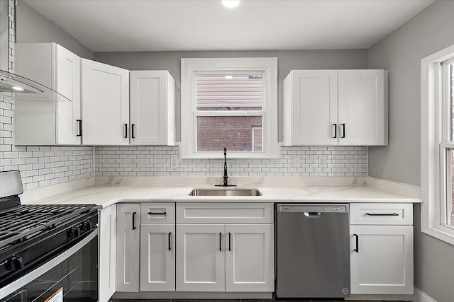 kitchen with appliances with stainless steel finishes, white cabinetry, sink, decorative backsplash, and wall chimney exhaust hood