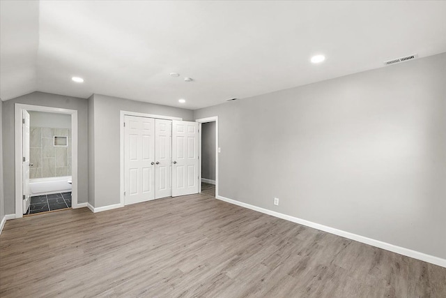 unfurnished bedroom with ensuite bathroom, a closet, and light hardwood / wood-style flooring