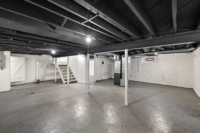 basement with brick wall, heating unit, and electric panel