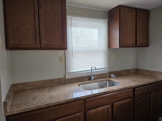 kitchen with dark brown cabinetry, light stone countertops, and sink