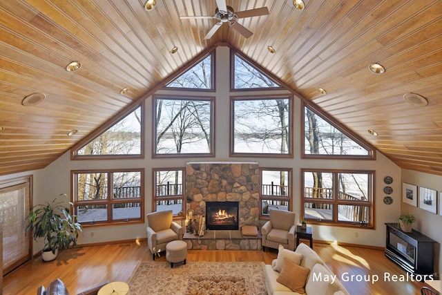 living room featuring wood ceiling, a stone fireplace, a high ceiling, and light wood-type flooring