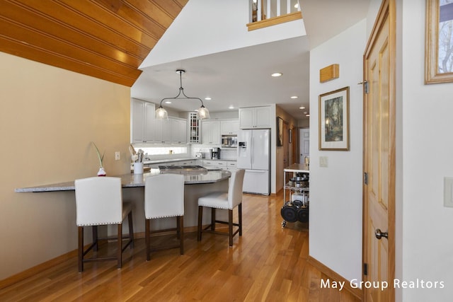 kitchen featuring white cabinetry, light stone counters, white refrigerator with ice dispenser, a kitchen bar, and kitchen peninsula