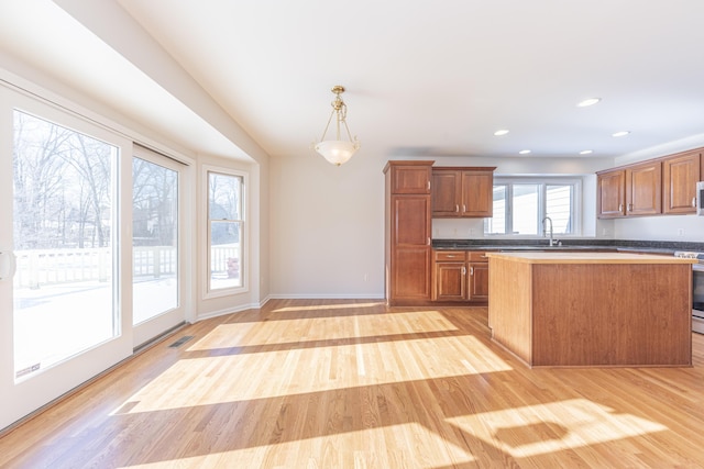 kitchen featuring hanging light fixtures, sink, stainless steel range, and light hardwood / wood-style floors