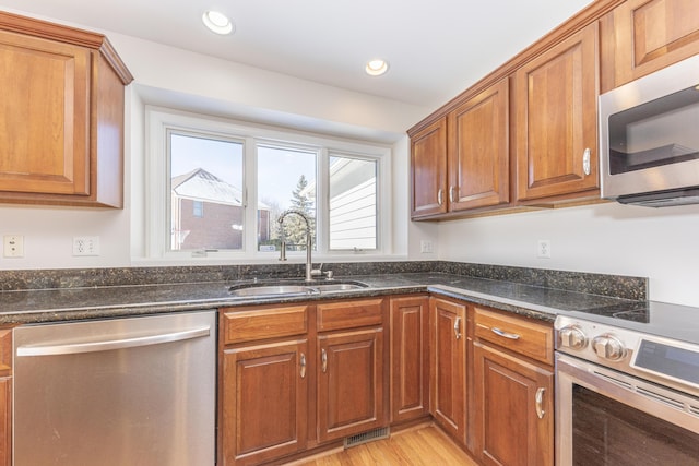 kitchen with appliances with stainless steel finishes, sink, dark stone countertops, and light hardwood / wood-style flooring