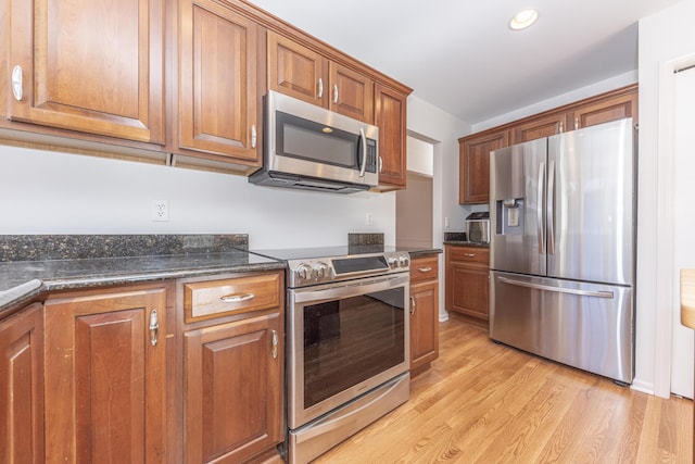 kitchen with appliances with stainless steel finishes, light hardwood / wood-style floors, and dark stone countertops