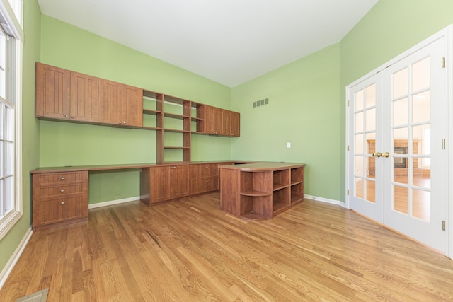 unfurnished office featuring french doors, built in desk, light hardwood / wood-style flooring, and a wealth of natural light