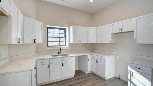 kitchen with light stone countertops, sink, white cabinets, and light wood-type flooring