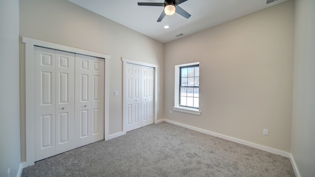 unfurnished bedroom with light carpet, two closets, and ceiling fan